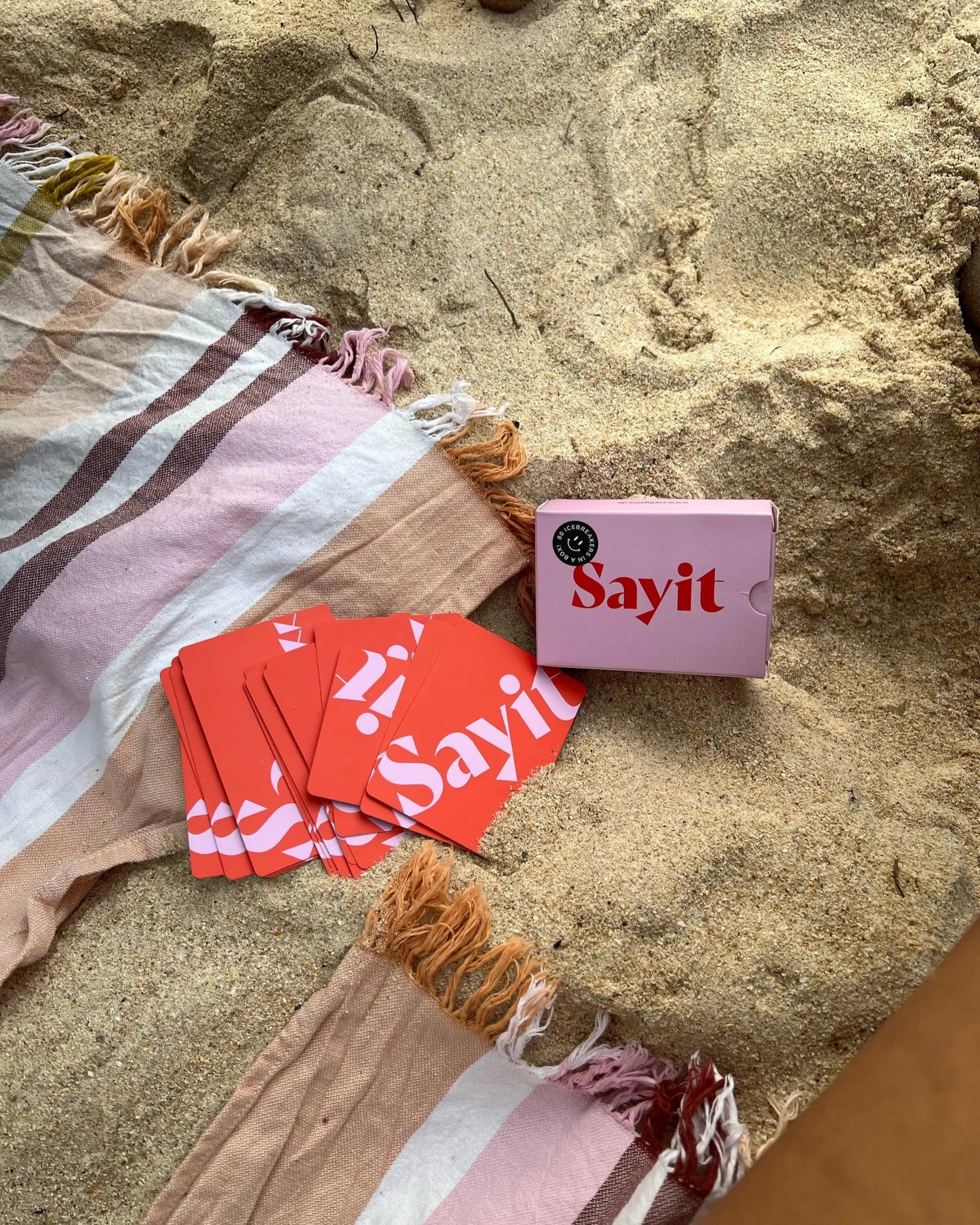 SAYIT Karten-Set liegt auf einem Handtuch im Sand, bereit für inspirierende Gespräche.
