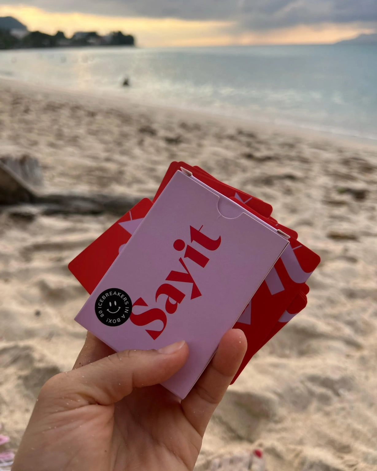 SAYIT Kartenspiel wird in der Hand gehalten, mit Blick auf das Meer und den Sonnenuntergang.