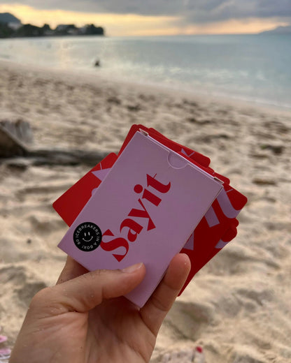 SAYIT Kartenspiel wird in der Hand gehalten, mit Blick auf das Meer und den Sonnenuntergang.