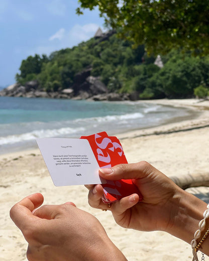 Hands-on: SAYIT Kartenspiel in Aktion – Person hält eine Fragekarte in der Hand, ideal für tiefgründige Gespräche am Strand.
