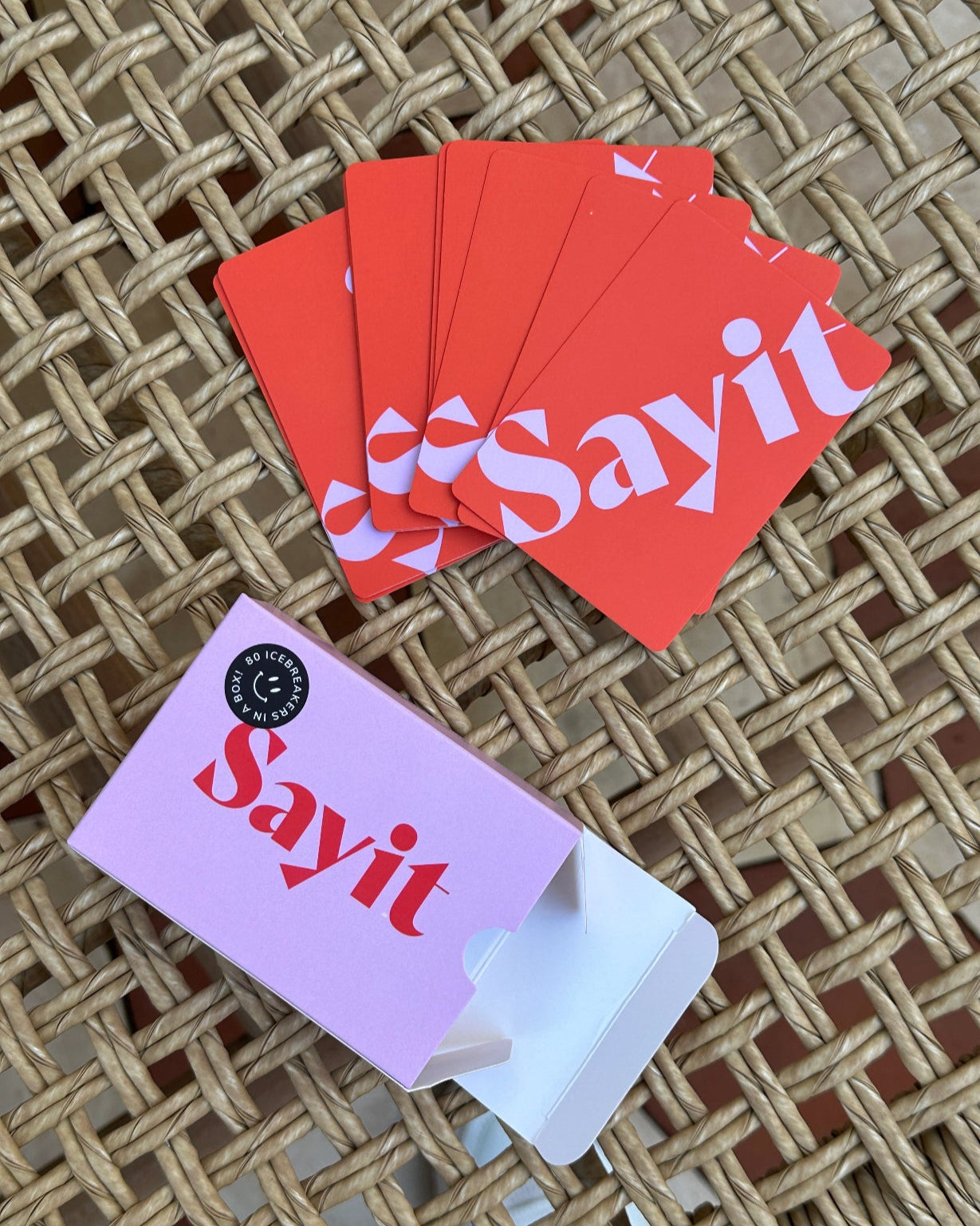 Close-up des SAYIT Kartenspiels – mediterranes Ambiente mit Detailansicht der Karten und Verpackung auf einem Rattan-Tisch.
